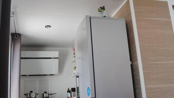 Una cucina compatta con mobili bianchi, un frigorifero in acciaio inox e una parete decorata in legno.