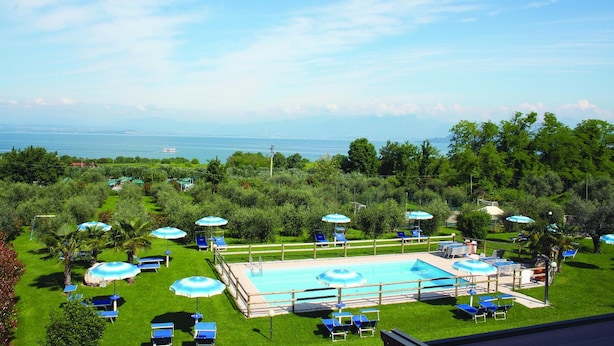 A pool area with sun loungers and umbrellas, surrounded by greenery and a view of the sea. - Agriturismo il giardino degli ulivi (Cortona)
