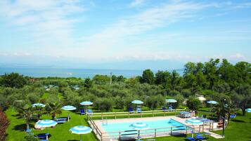 Area piscina con lettini e ombrelloni, immersa nel verde e con vista sul mare.