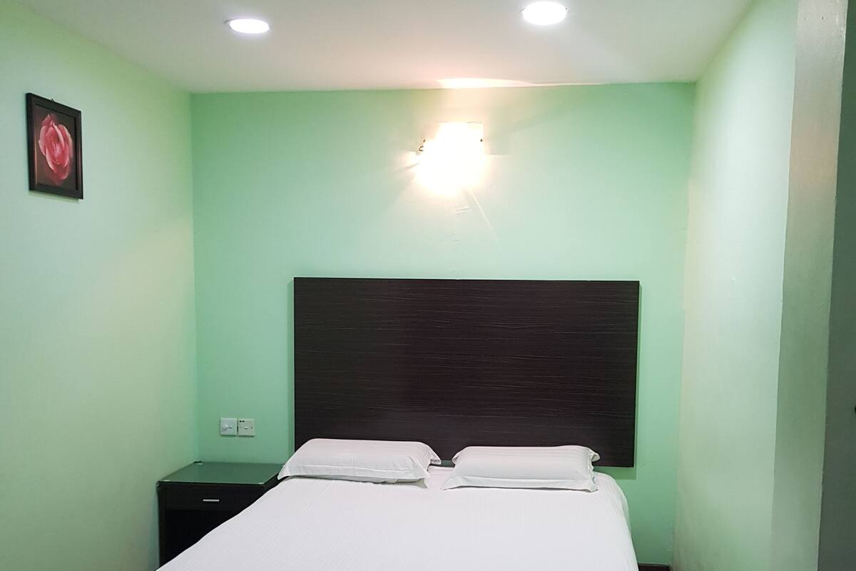 A room with a bed, a nightstand, a wall-mounted light, and a framed picture.