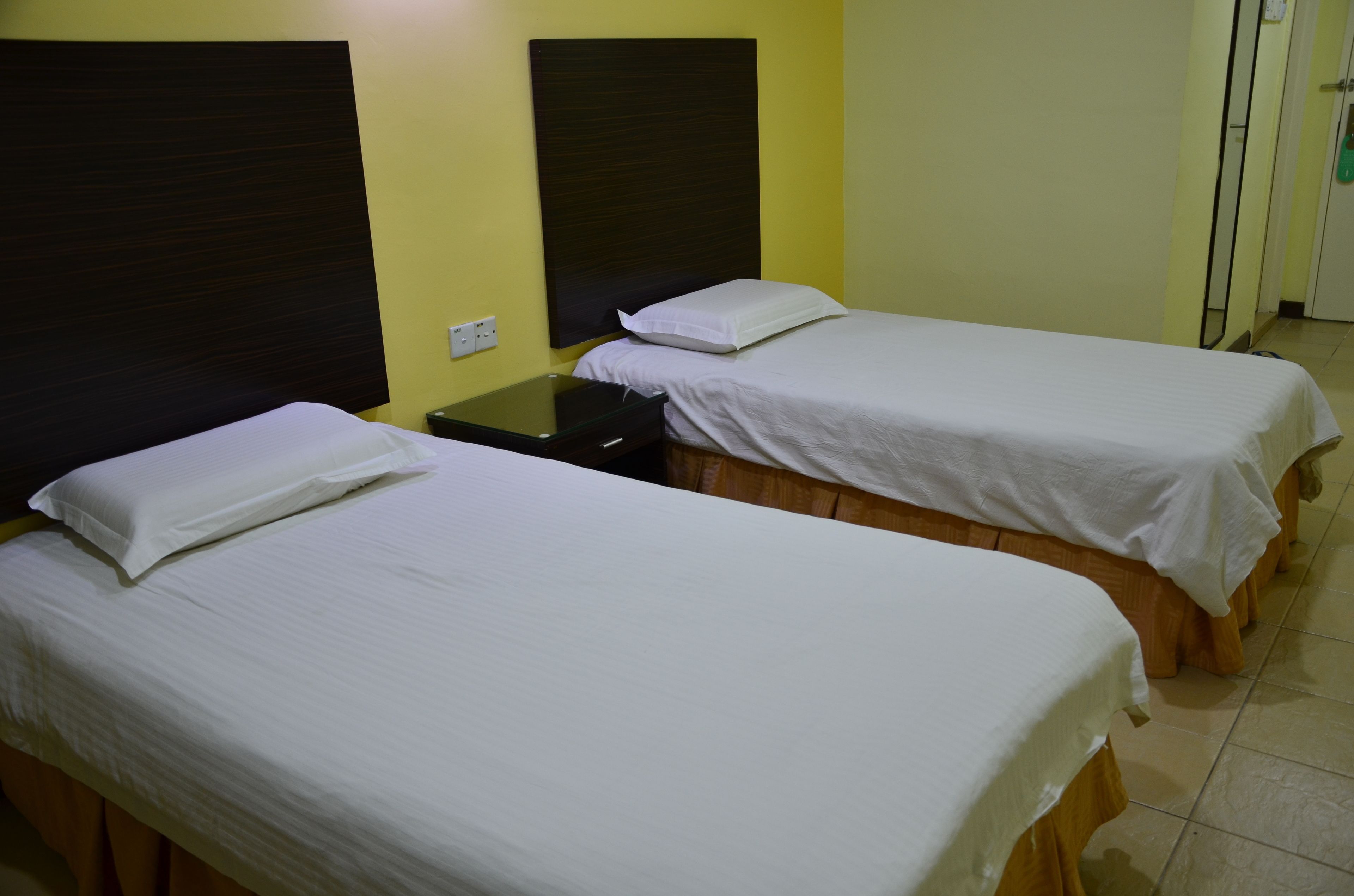 Two single beds with wooden headboards and white bedding in a room with yellow walls.
