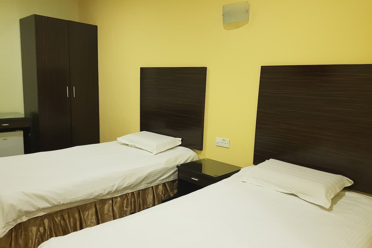 A hotel room with two single beds, a wardrobe, and a small desk.
