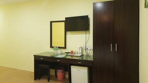 Una habitación pequeña con escritorio, espejo, televisión, armario y un refrigerador pequeño.