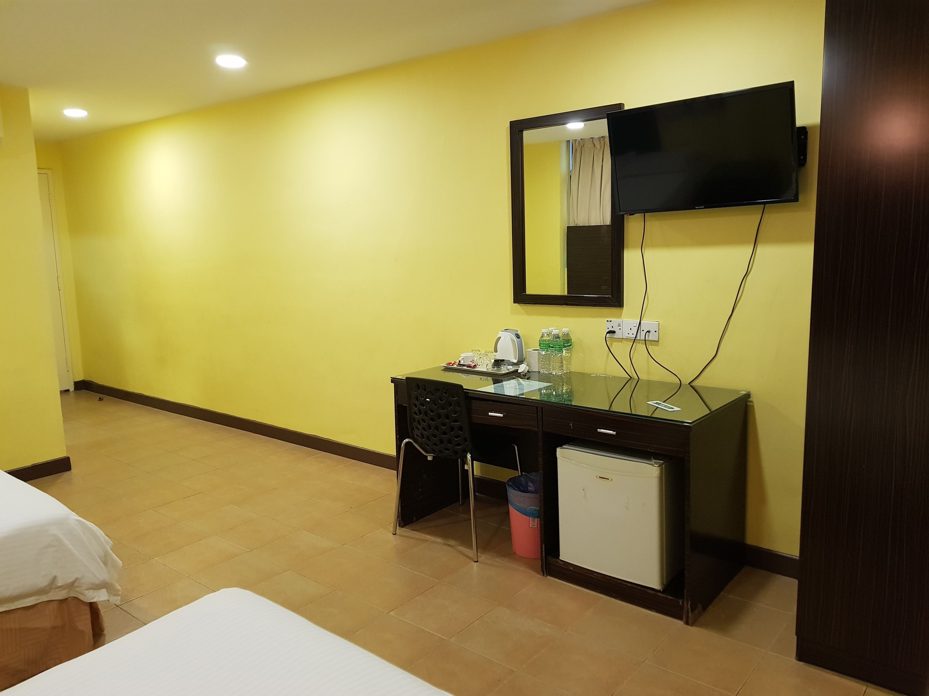 Una habitación de hotel con una cama, un escritorio con teléfono, un refrigerador pequeño y un televisor montado en la pared.