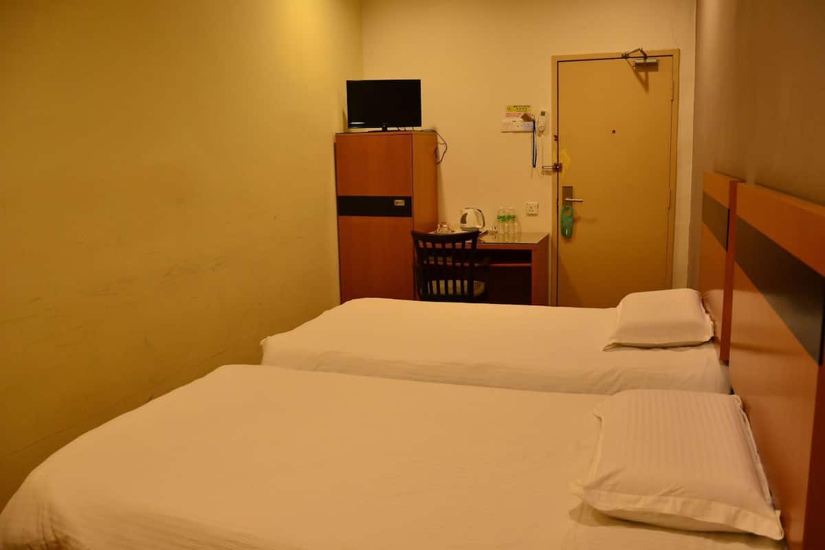 A hotel room with two beds, a desk with a chair, a television on a cabinet, and a door with a lock.