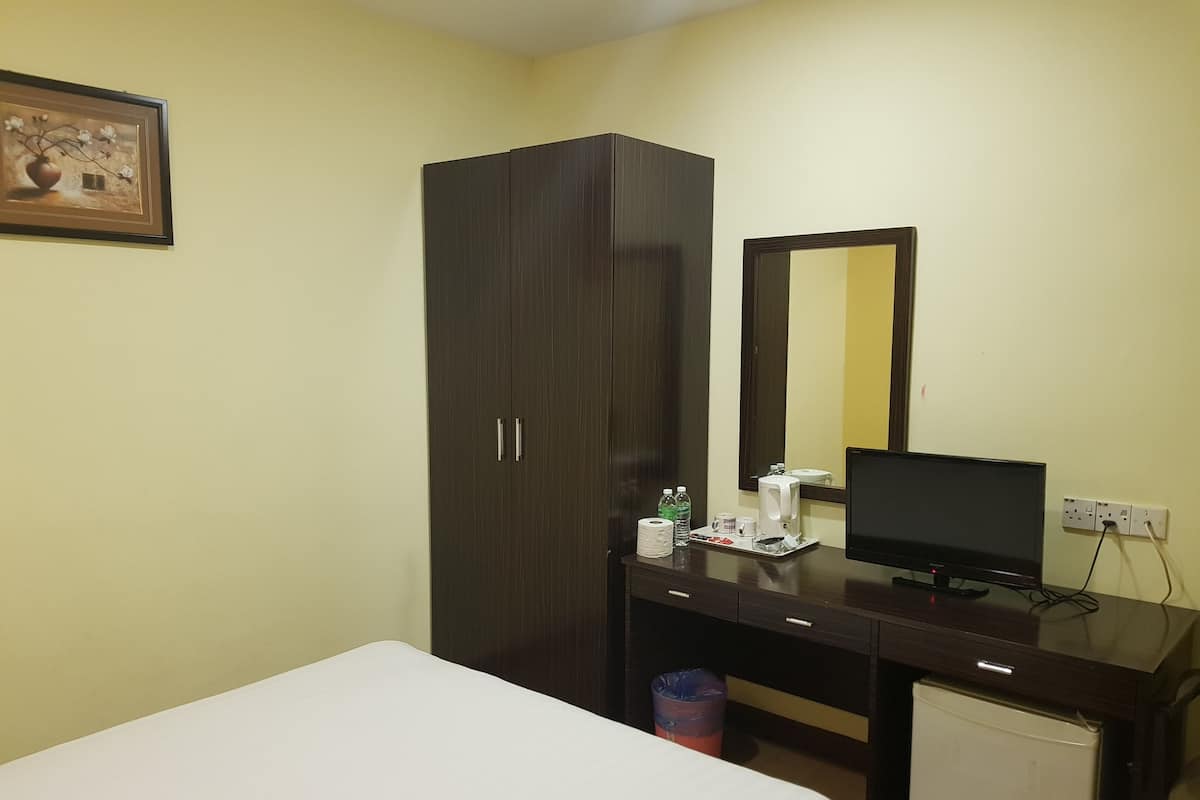 A hotel room with a bed, a desk with a computer, a wardrobe, and a mirror.