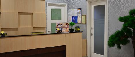 A reception area with a wooden counter, a bulletin board, a potted plant, and a door.