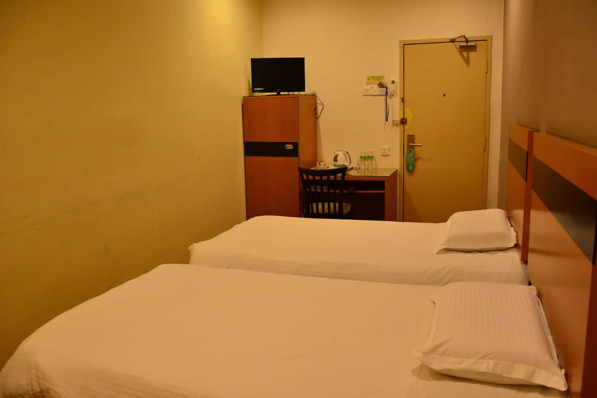 A small hotel room with two beds, a desk with a chair, a television on top of a wardrobe, and a door with a lock and a phone.