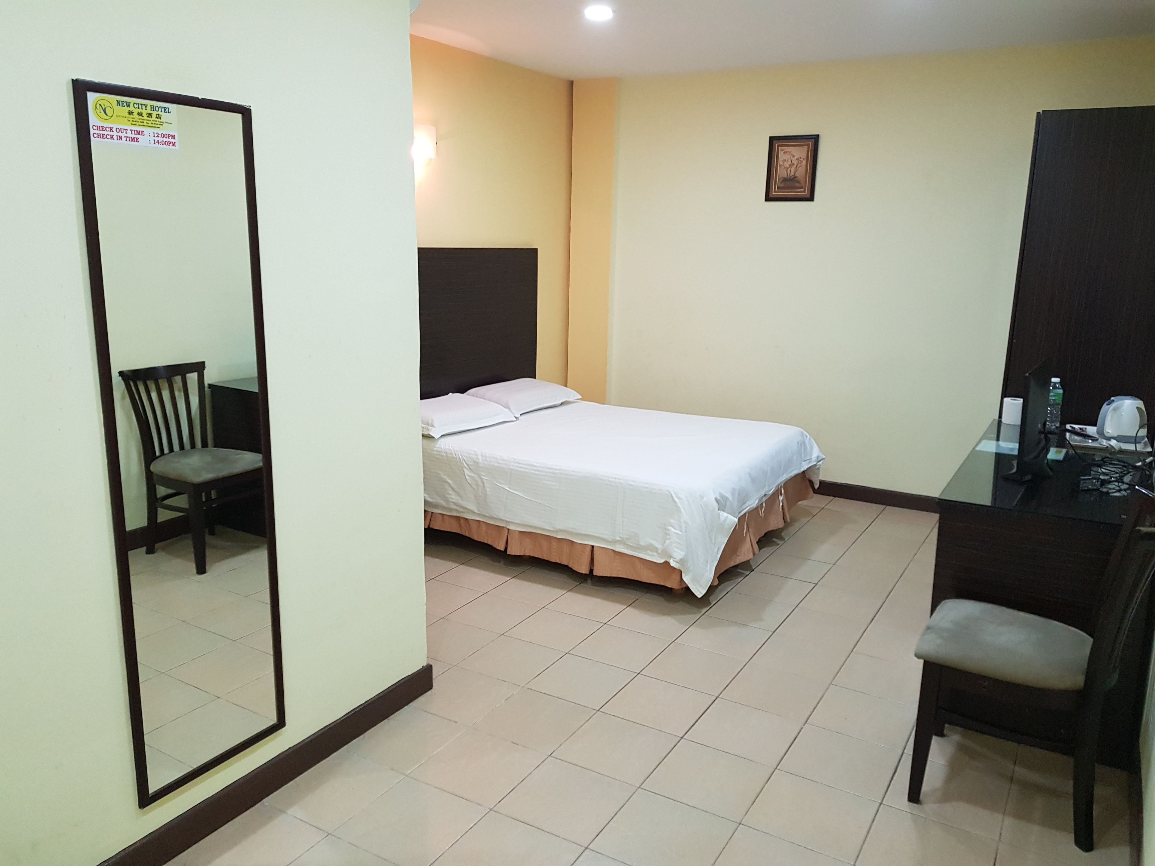 A hotel room with a bed, a desk, a chair, a mirror, and a wall-mounted picture.