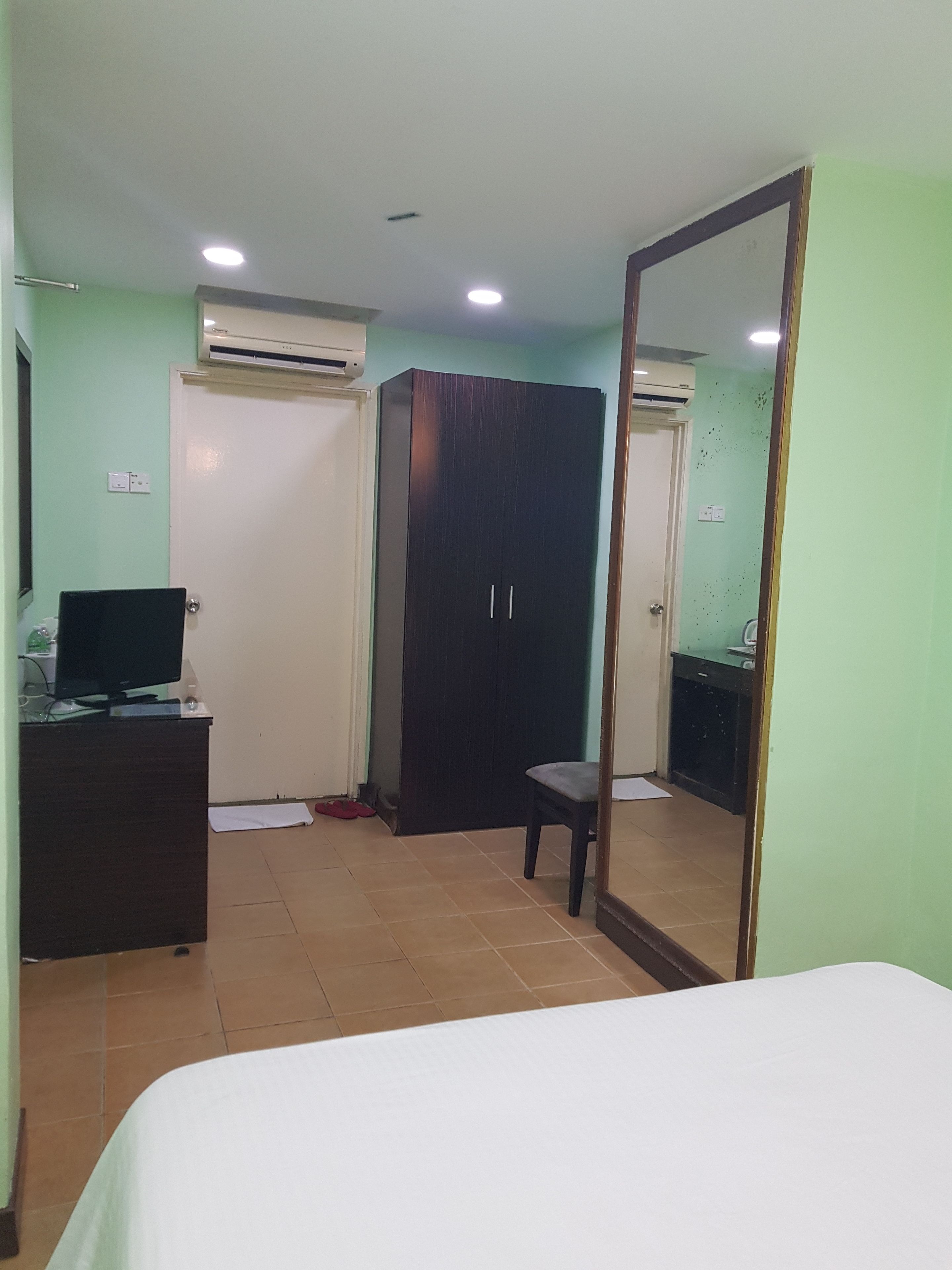 A hotel room with a bed, a desk with a computer, a wardrobe, and a mirror.