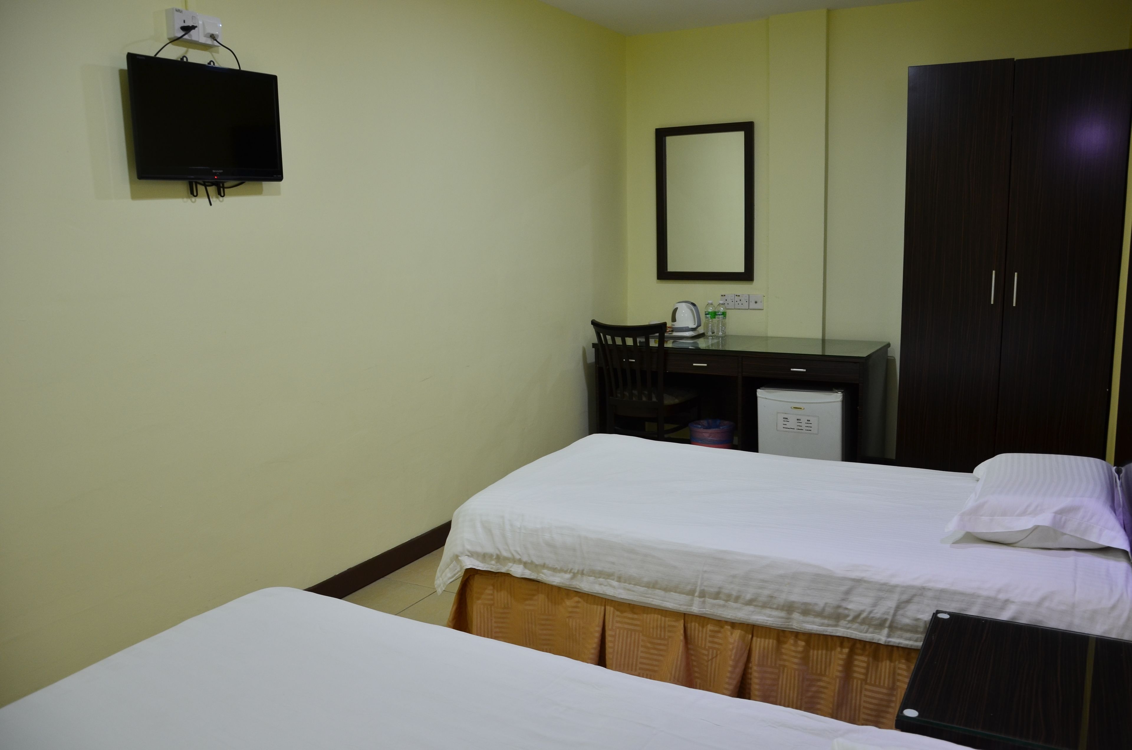 A hotel room with a bed, a desk with a chair, a wardrobe, and a television mounted on the wall.