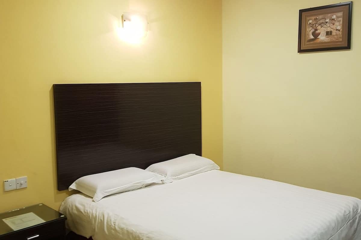 A hotel room with a bed, a nightstand, a wall-mounted light, and a framed picture.