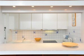 Cozinha moderna com armários brancos, bancada clara e painel de azulejos azuis.