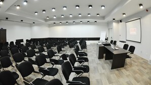 A conference room with rows of black chairs, a long table with a laptop, and a projector screen on the wall. - Hotel Putnik (Novi Sad)