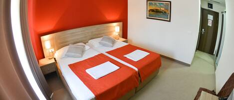 A hotel room with a double bed, two pillows, a nightstand, a lamp, and a painting on the wall.