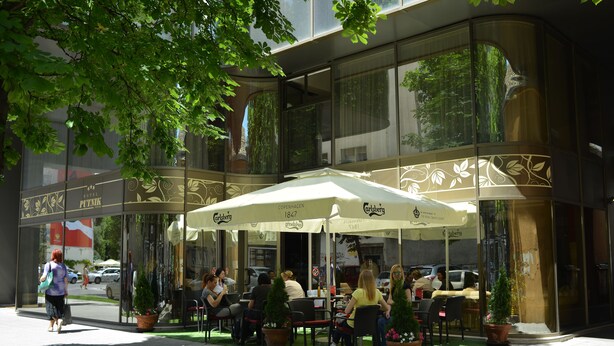 An outdoor cafe with tables and chairs, surrounded by potted plants. - Hotel Putnik (Novi Sad)