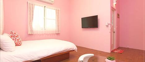 Un dormitorio con decoración rosa, una cama, un televisor, una mesita de cristal y una puerta.