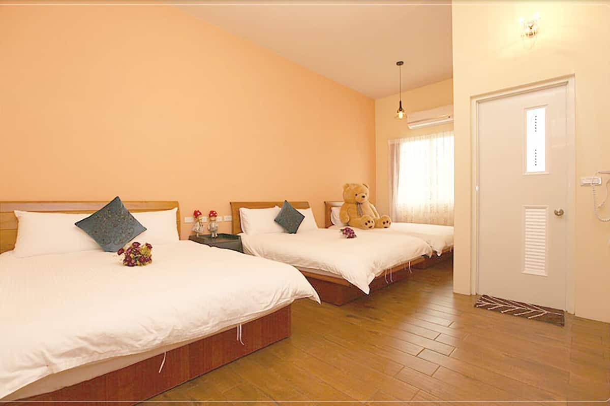 A hotel room with two beds, wooden flooring, a teddy bear on one bed, and a door with a window.