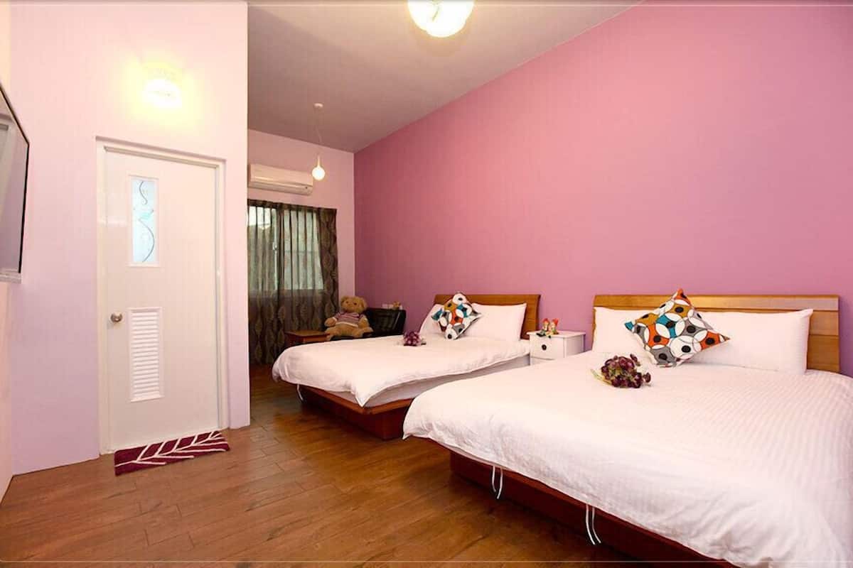 A hotel room with two beds, a wooden floor, a pink wall, and a white door.