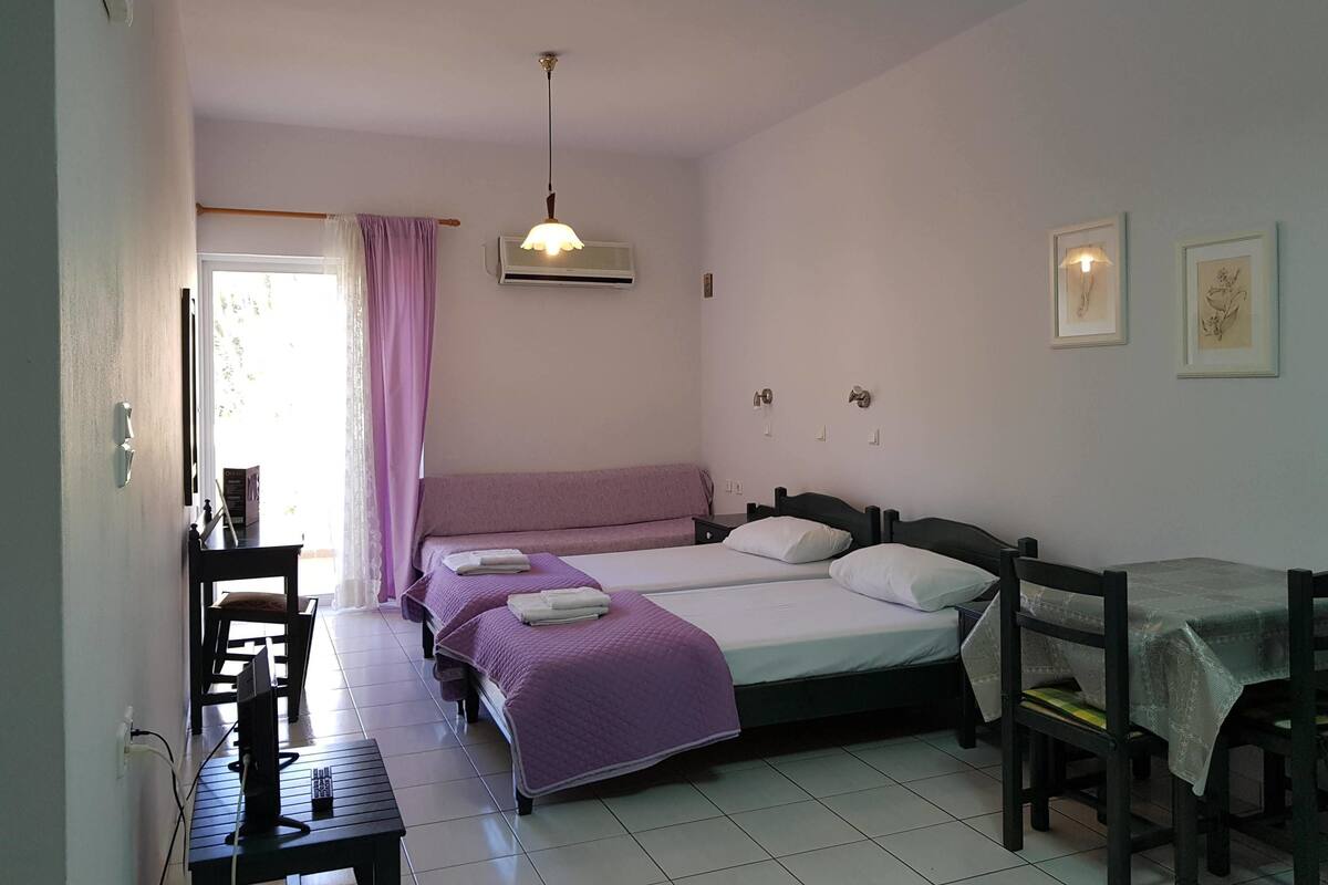 A bedroom with two beds, a desk, a chair, an air conditioning unit, and a window with curtains.