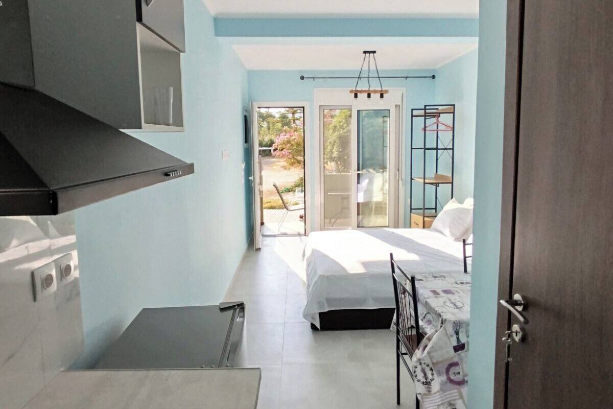 A compact room with a bed, a kitchenette, and a door leading to an outdoor area.