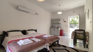 A hotel room with two beds, a kitchenette, and a chair with a table. - Zinovia (Chania)