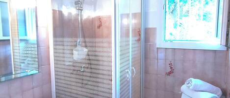 A bathroom with a glass-enclosed shower, a sink, and a window with a view of trees.