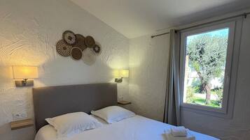 Une chambre d’hôtel avec un grand lit, deux lampes de chevet, un élément décoratif fixé au mur et une fenêtre donnant sur un paysage verdoyant.