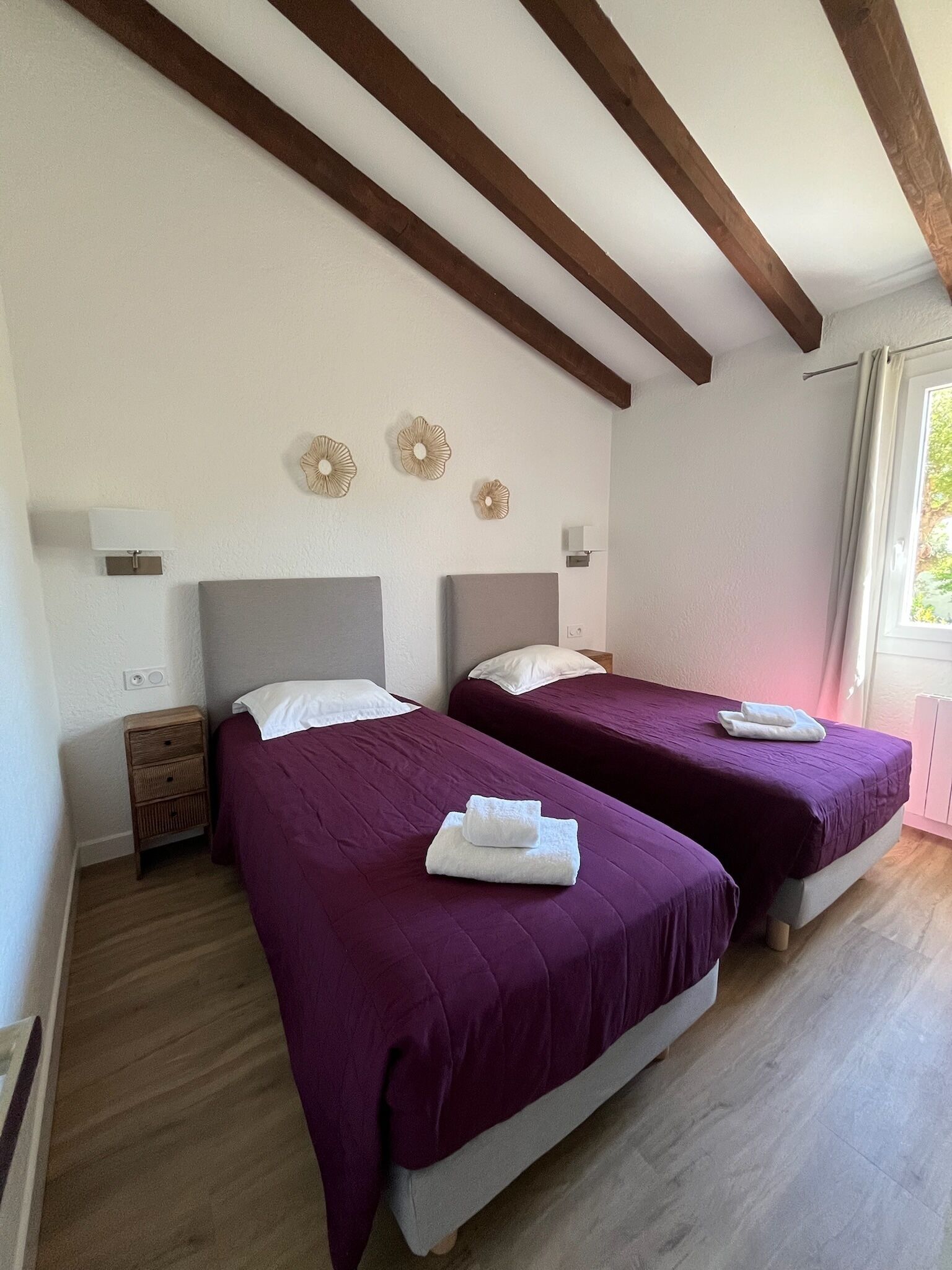Una habitación con dos camas, vigas de madera en el techo y una ventana con cortinas.