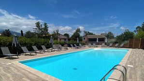 A rectangular swimming pool with a wooden deck surrounding it, equipped with lounge chairs and umbrellas. - Residence Les Cigales (Porto-Vecchio)
