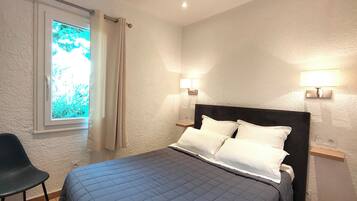 A bedroom with a bed, two bedside lamps, a window with curtains, and a chair.