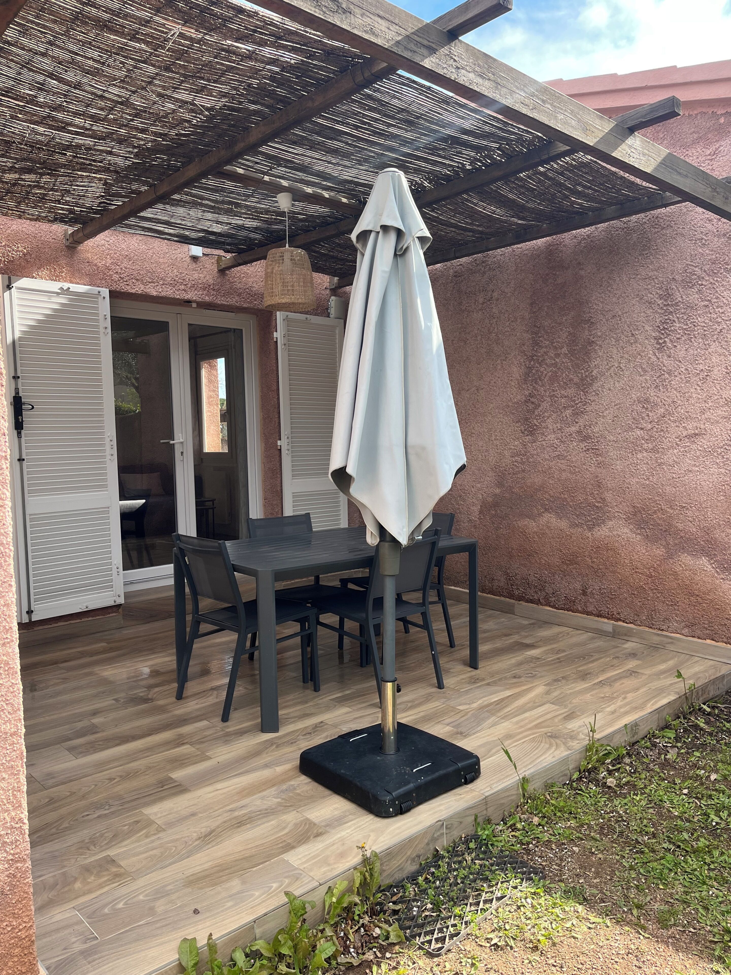 An outdoor patio with a table and chairs, a covered area with a woven ceiling, and a door leading to an interior space.