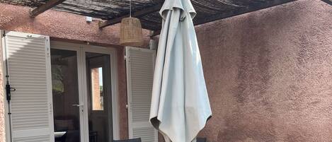An outdoor patio with a table and chairs, a covered area with a woven ceiling, and a door leading to an interior space.