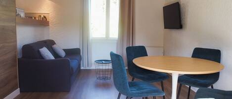 Ein modernes Wohnzimmer mit einer Couch, einem runden Esstisch und blauen Stühlen.