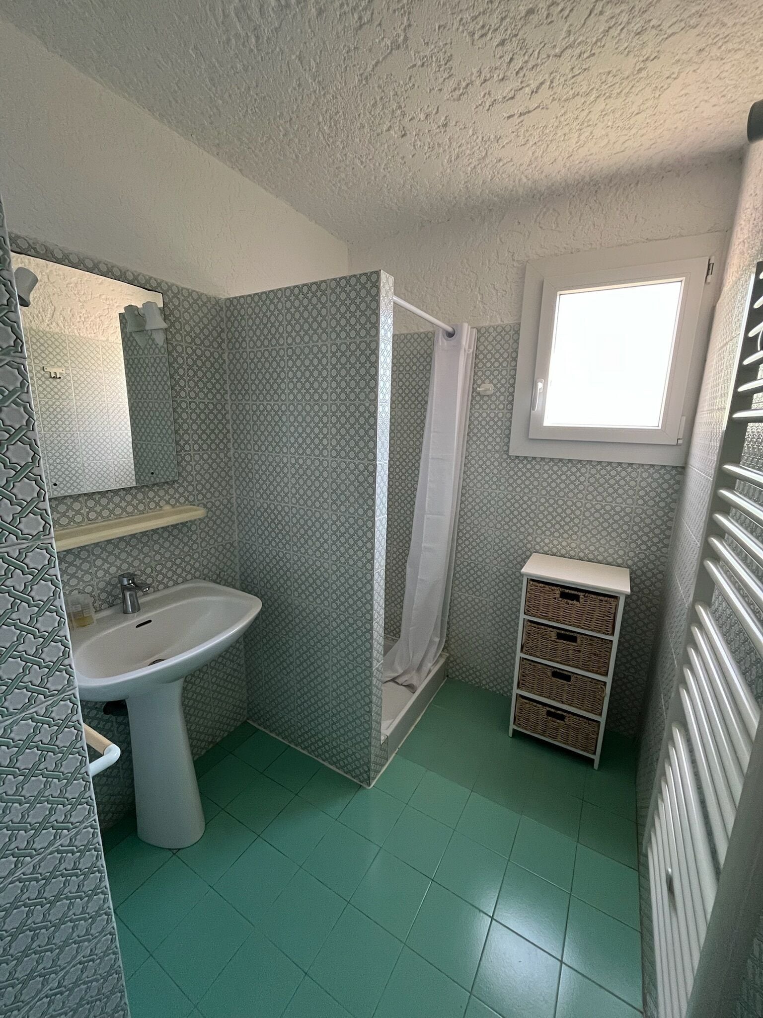 A bathroom with a sink, mirror, shower, and a window.