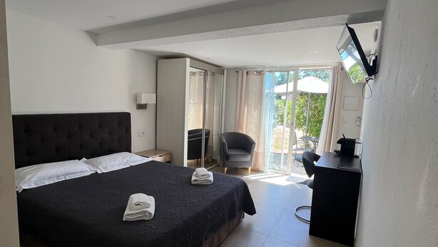 A hotel room with a large bed, a desk, a chair, and a view of the outdoors. - Residence Les Cigales (Porto-Vecchio)