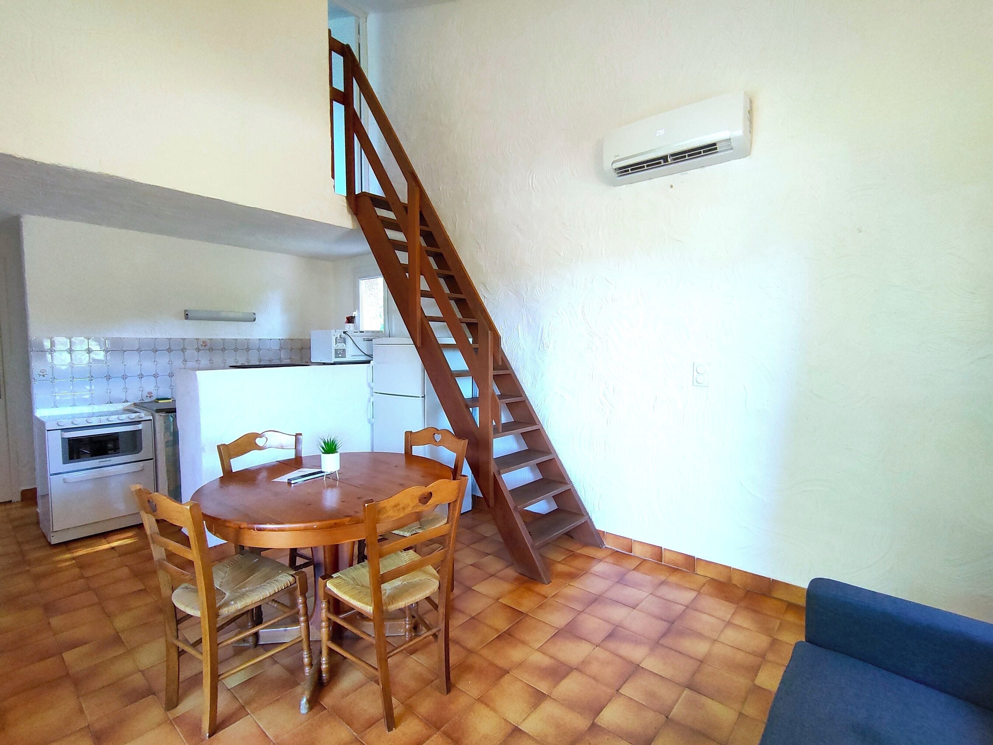 A compact kitchen with a wooden table and chairs, a staircase, and a blue sofa.