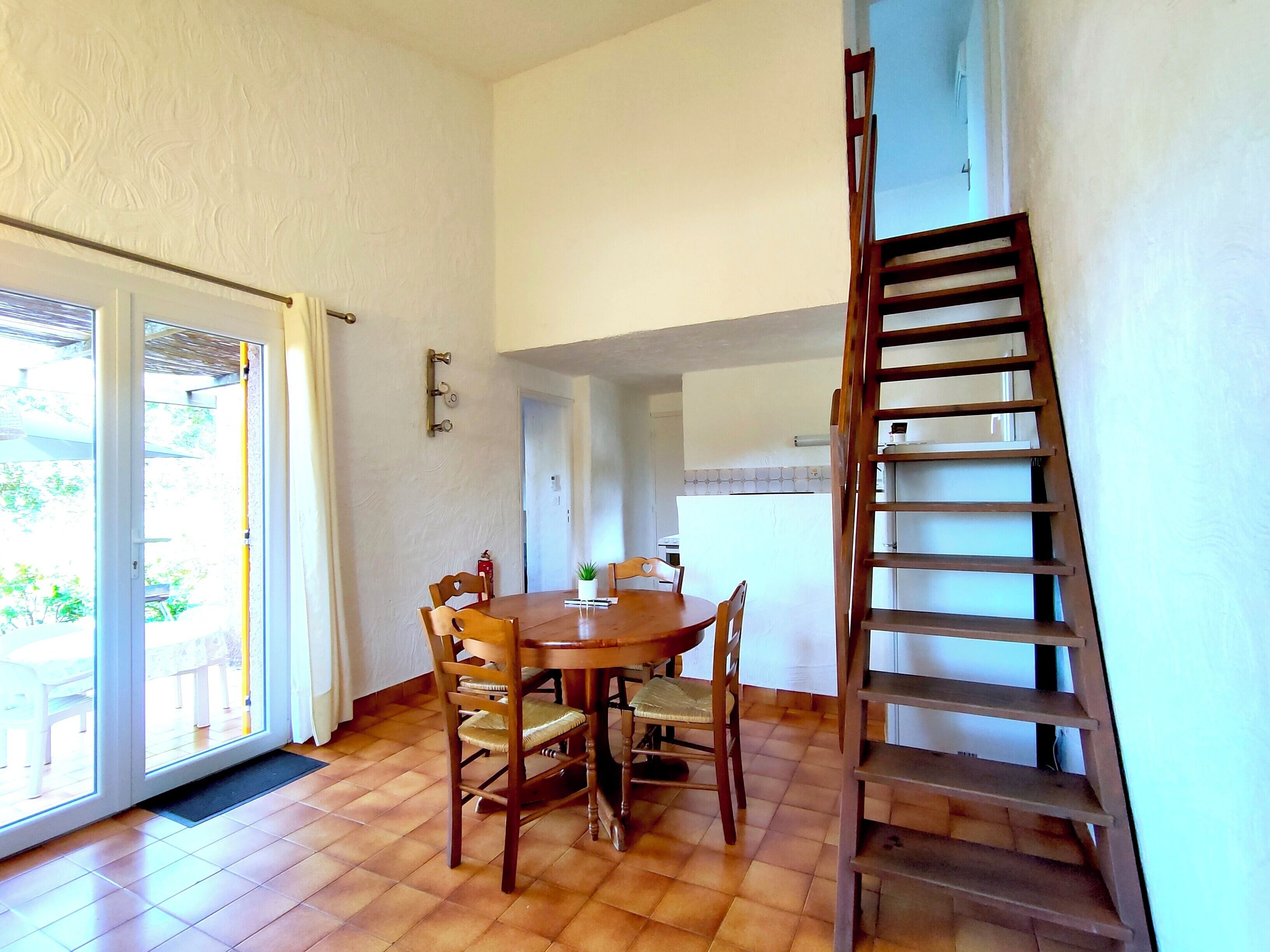 A dining area with a wooden table and chairs, a staircase, and a sliding glass door leading outside.