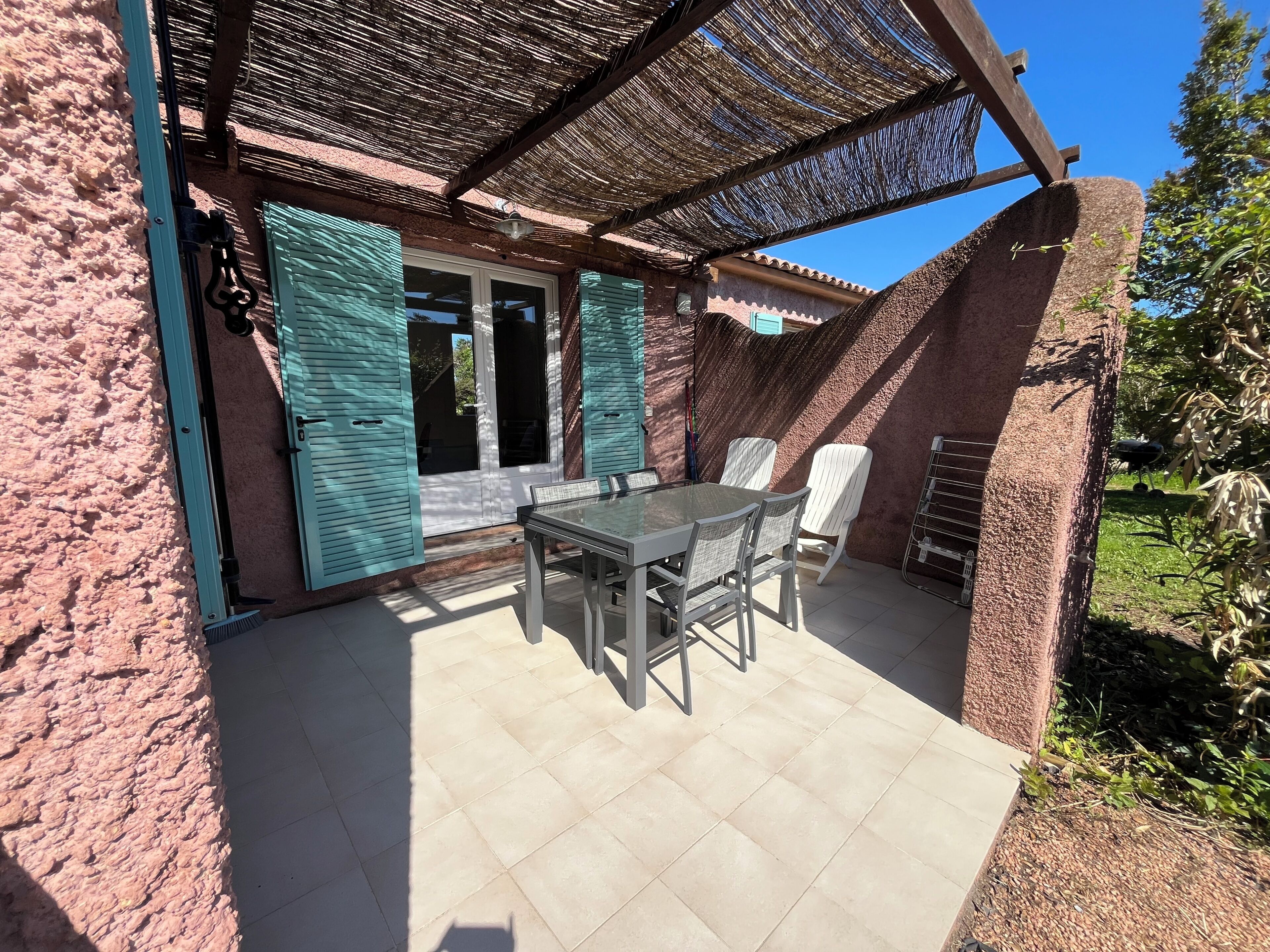 Une terrasse avec une table et des chaises, une porte et un espace abrité doté d’un toit de chaume.