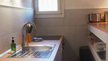 Een compacte keuken met een ingebouwde wasmachine, een raam boven de gootsteen en een klein aanrecht met een waterkoker.