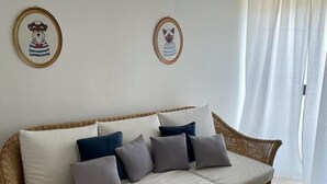 A wicker sofa with white cushions and multiple pillows in a room with white walls and a large window with sheer curtains. - Vista Mare Maratea B&B (Maratea)