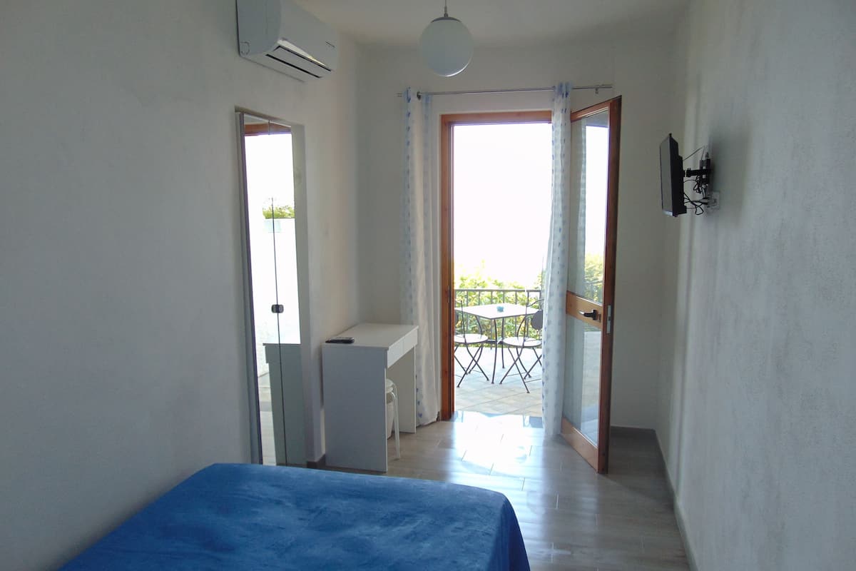Une chambre avec un lit, un bureau et une chaise. Il y a un balcon avec une table et des chaises.