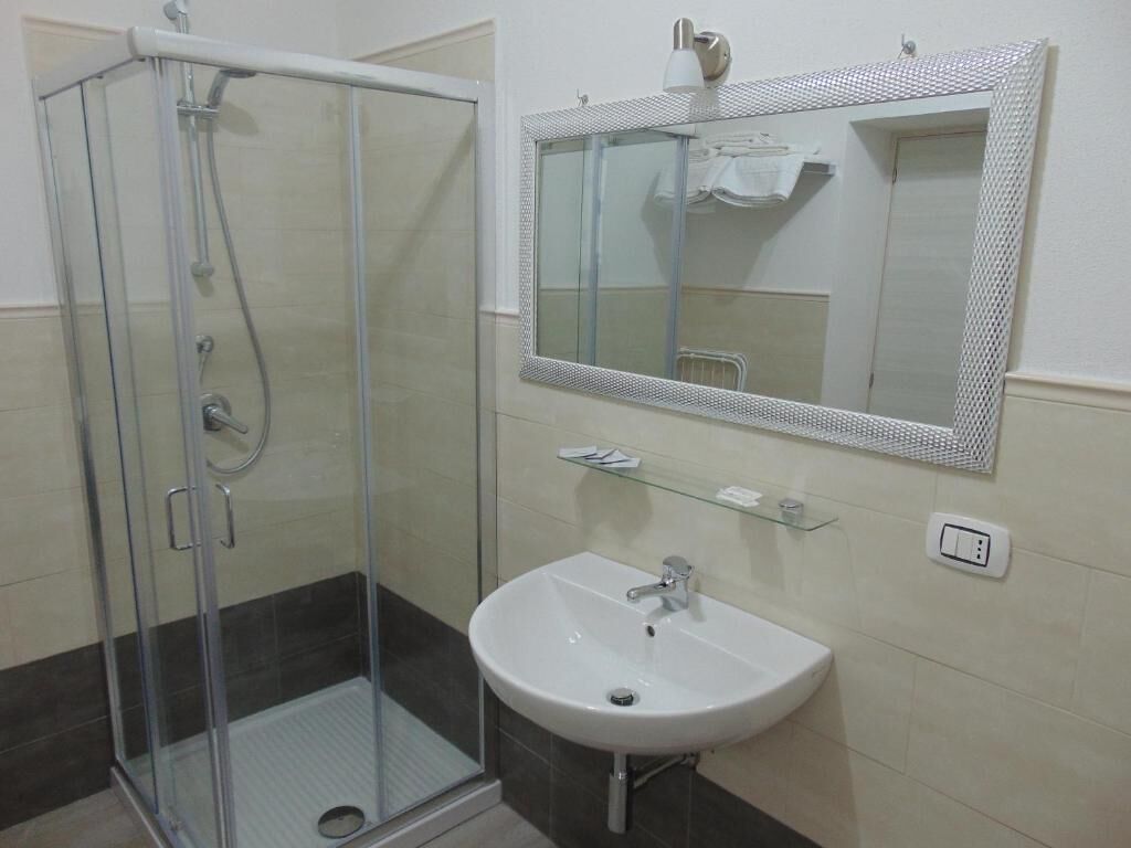 Un baño con cabina de ducha de vidrio, lavabo blanco y espejo con marco texturizado.