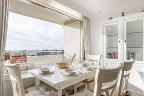Un coin repas avec une table dressée pour quatre personnes, des chaises, un panier de buffet et un buffet blanc aux portes vitrées.
