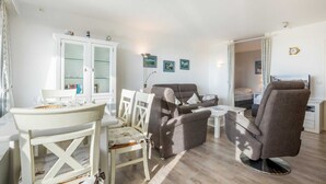 A living room with a white dining table, two armchairs, a sofa, and a cabinet.