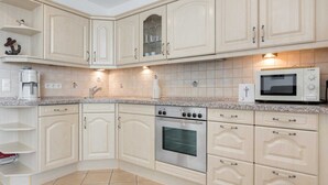 A kitchen with white cabinetry, a built-in oven, a microwave, and a coffee maker.