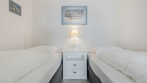 A twin room with two beds, a nightstand with a lamp, a framed picture on the wall, and a power outlet.