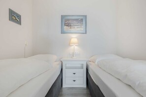 Une chambre double avec deux lits, une table de chevet avec une lampe, un tableau encadré au mur et une prise électrique.