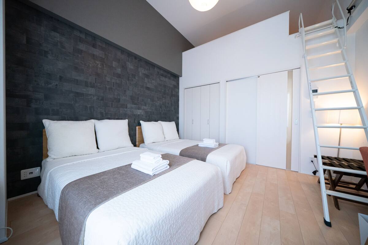 A modern hotel room with two beds, a dark textured wall, a white wardrobe, and a white ladder.