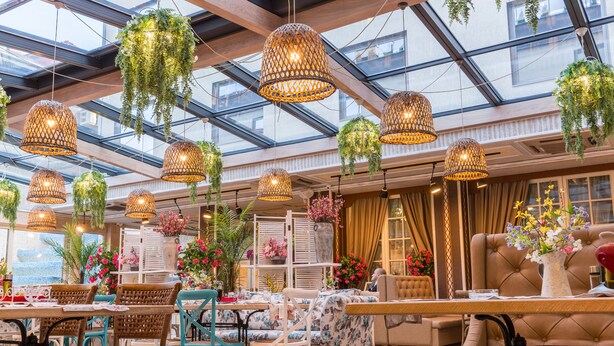 A spacious indoor area with hanging wicker lamps, comfortable seating, and a large window providing natural light.